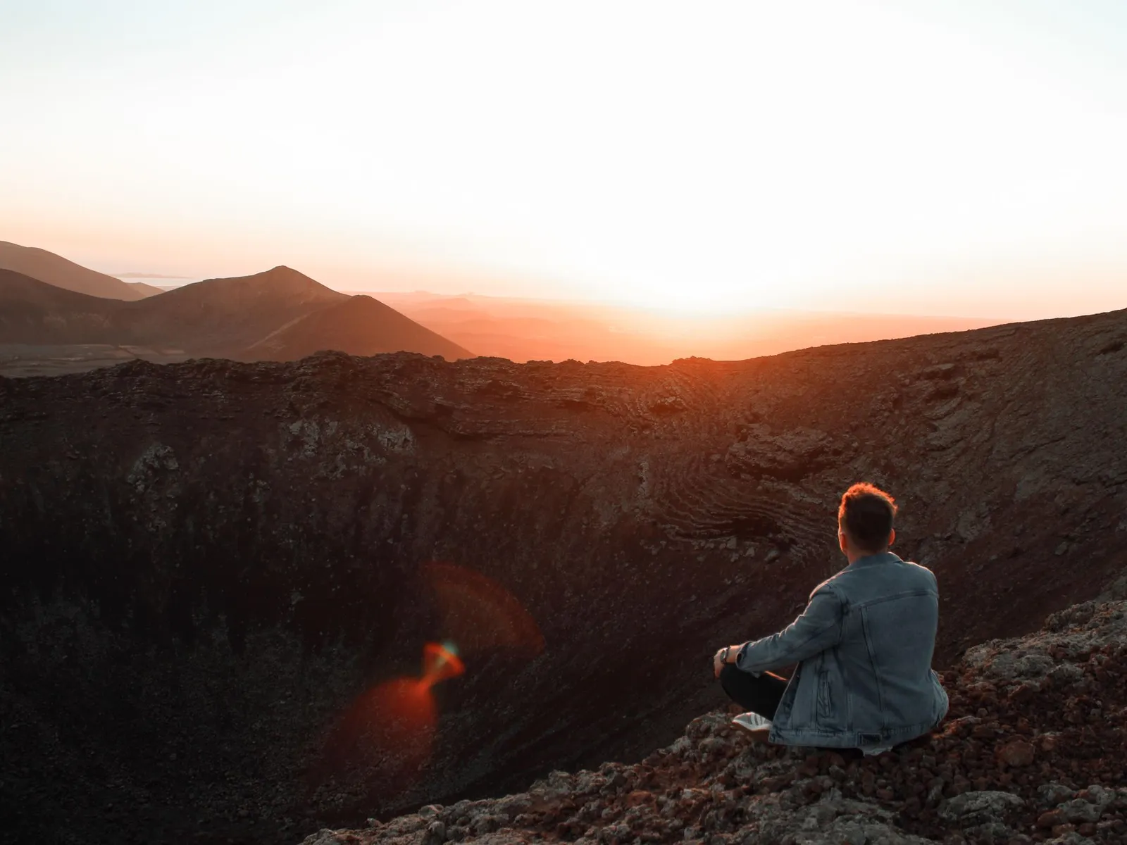 Senderista contemplando el atardecer desde el borde de un cráter volcánico