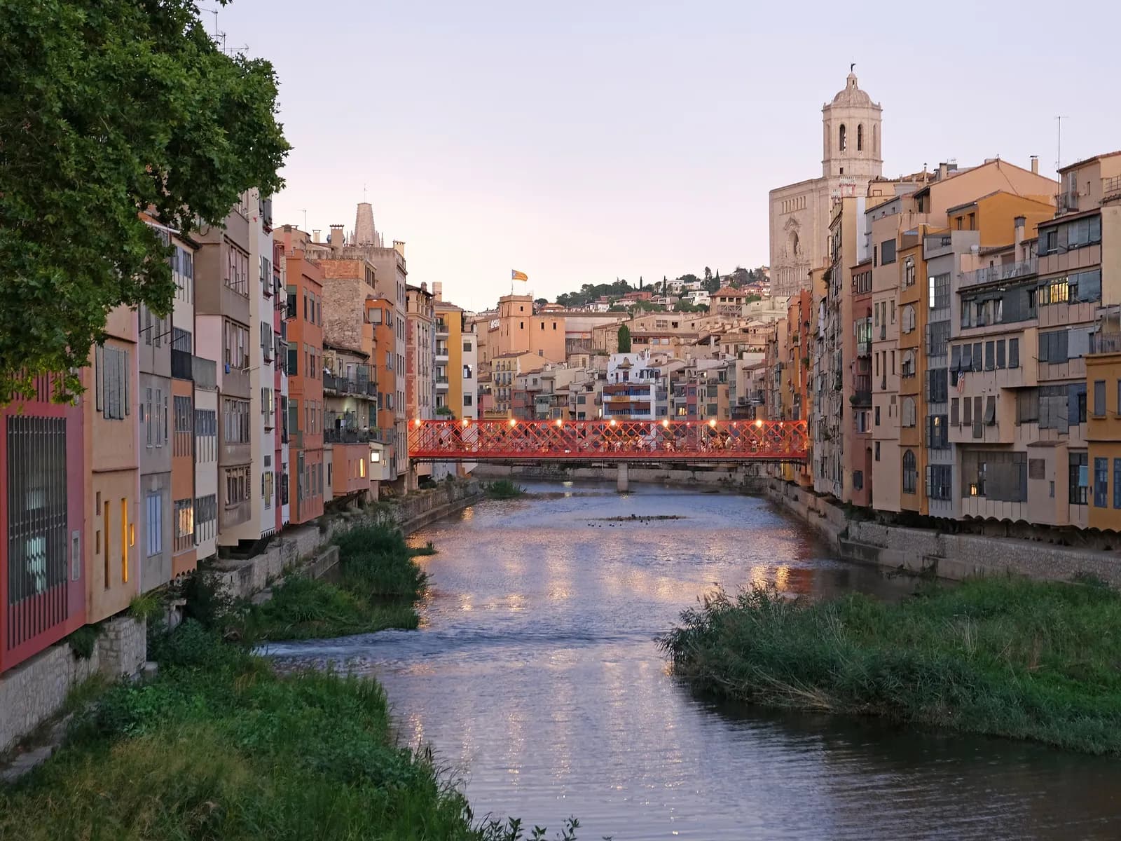 The Onyar river at dusk with the lit red bridge and Girona Cathedral behind