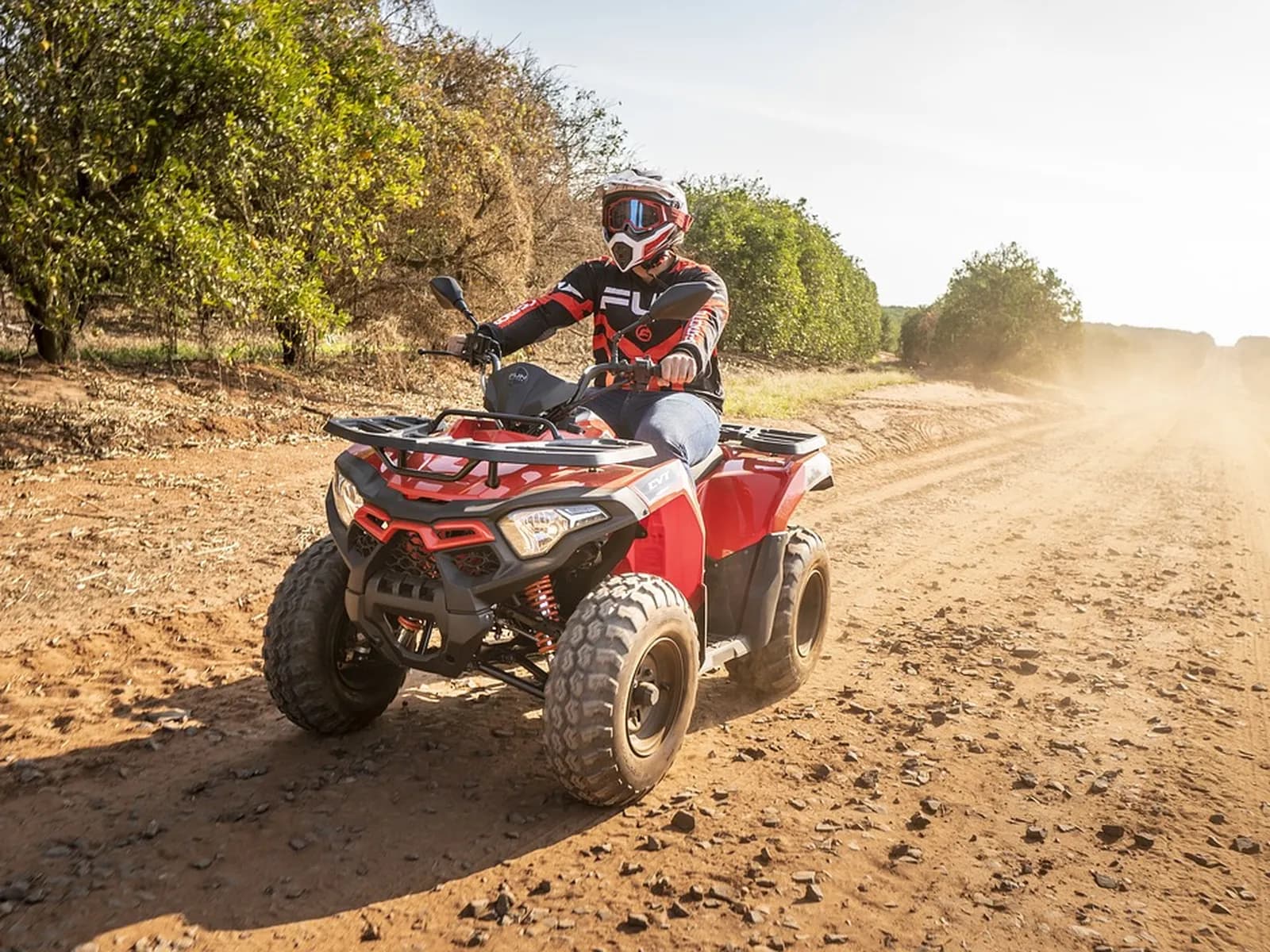 Quad rojo con piloto y casco por una pista de tierra
