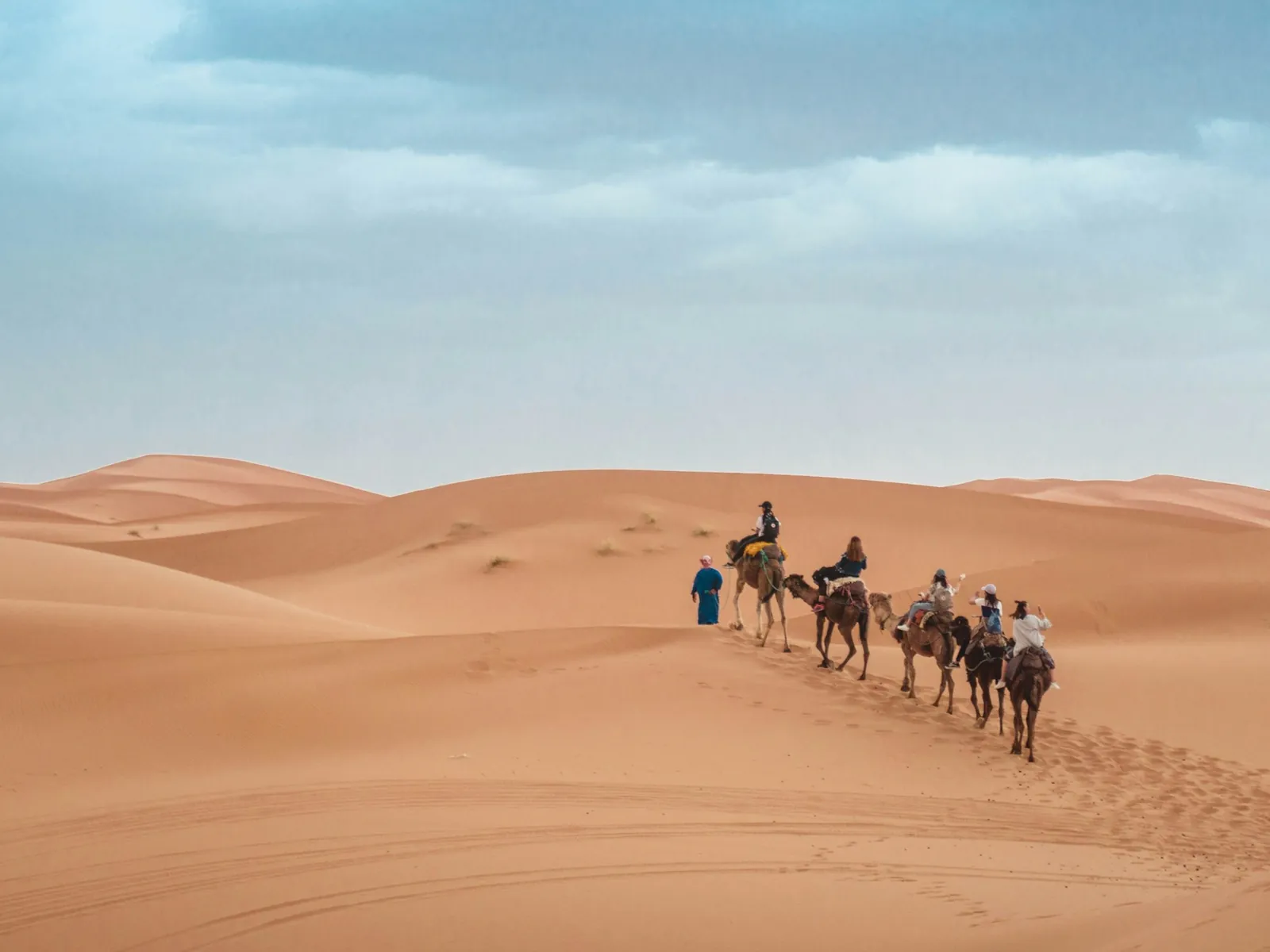 Caravana de camellos con jinetes cruzando unas dunas de arena