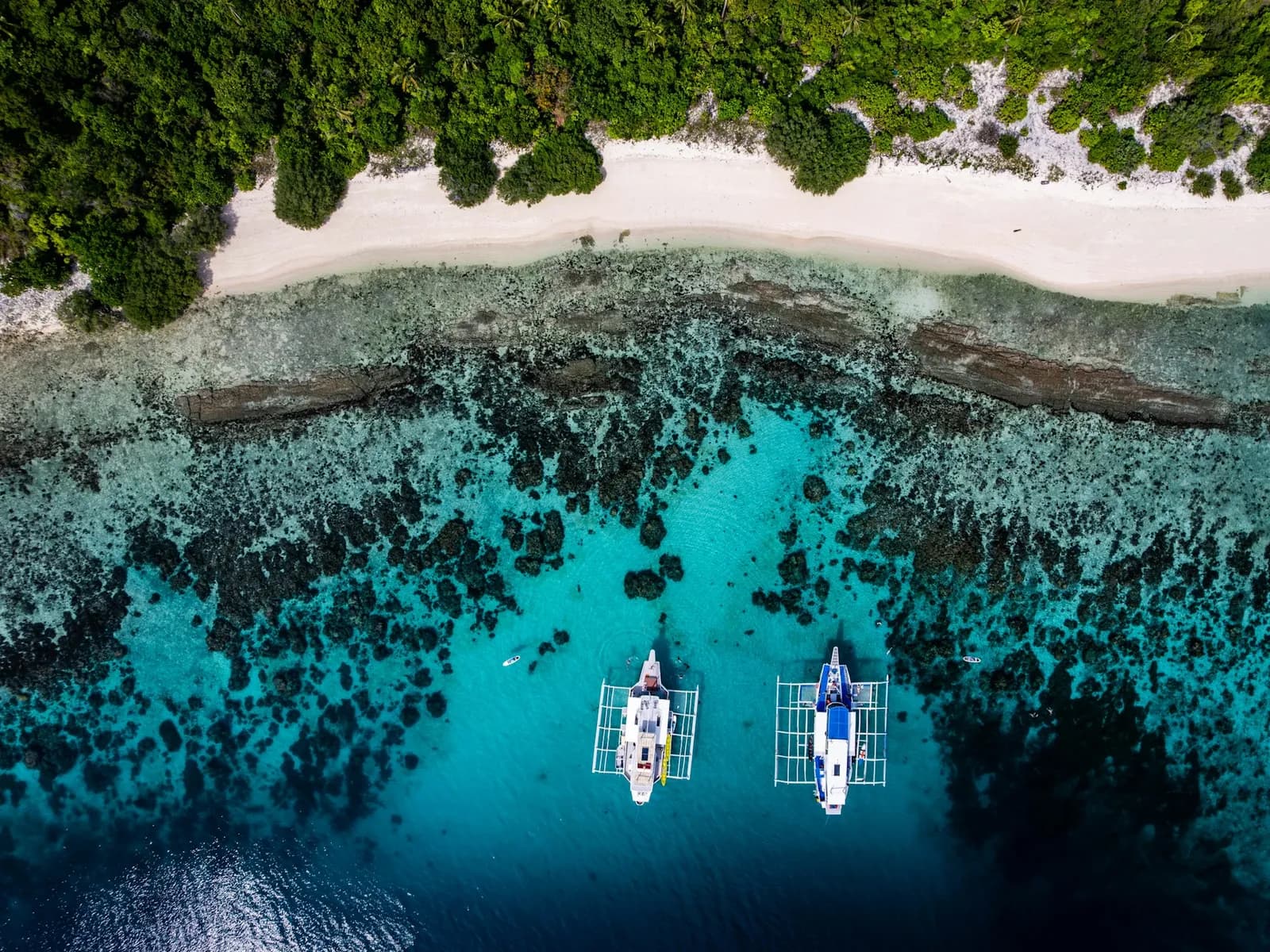 Catamaranes fondeados en aguas turquesa cerca de la orilla, vistos desde el aire