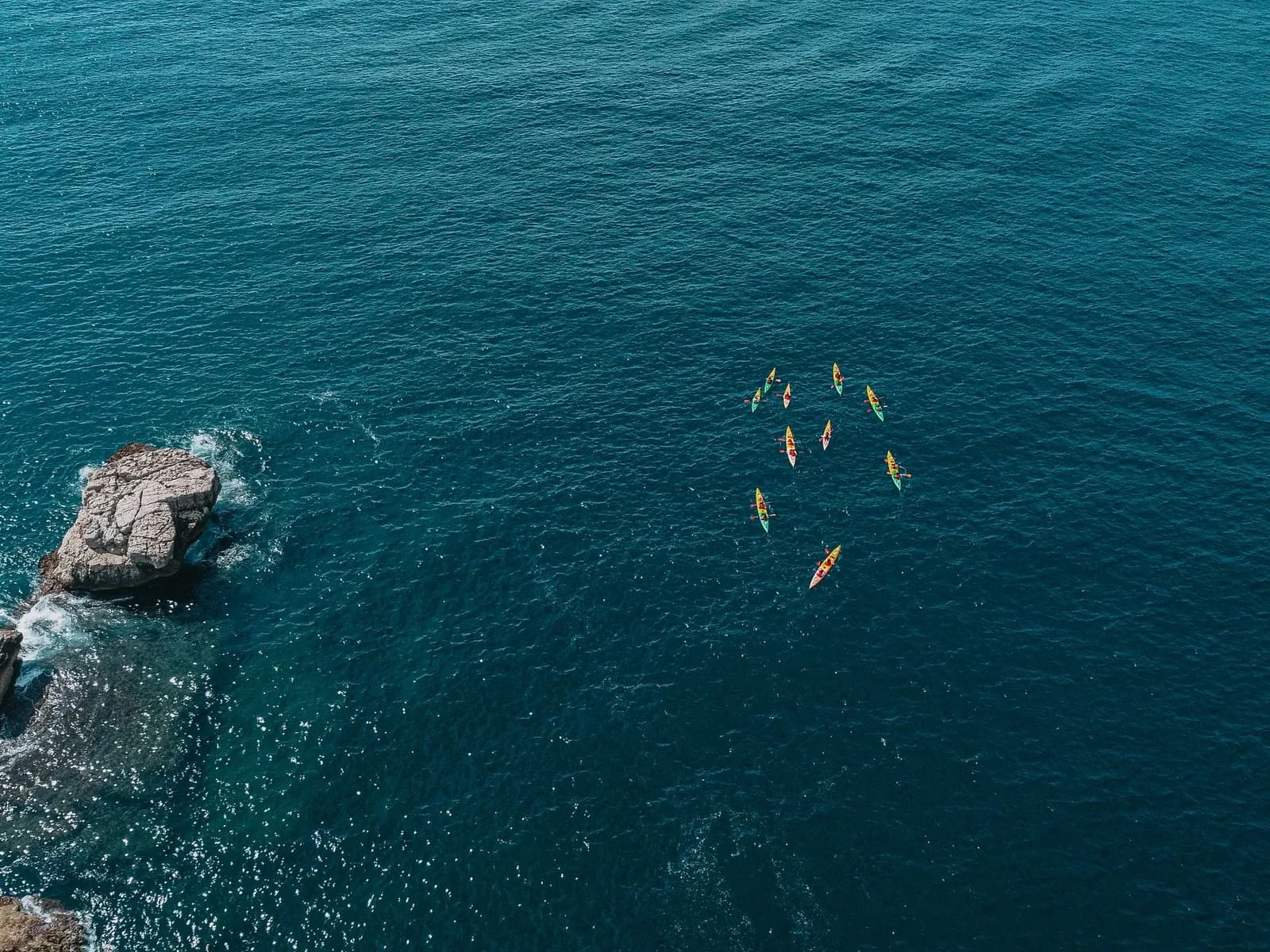 Aerial view of kayakers paddling along a rocky coastline