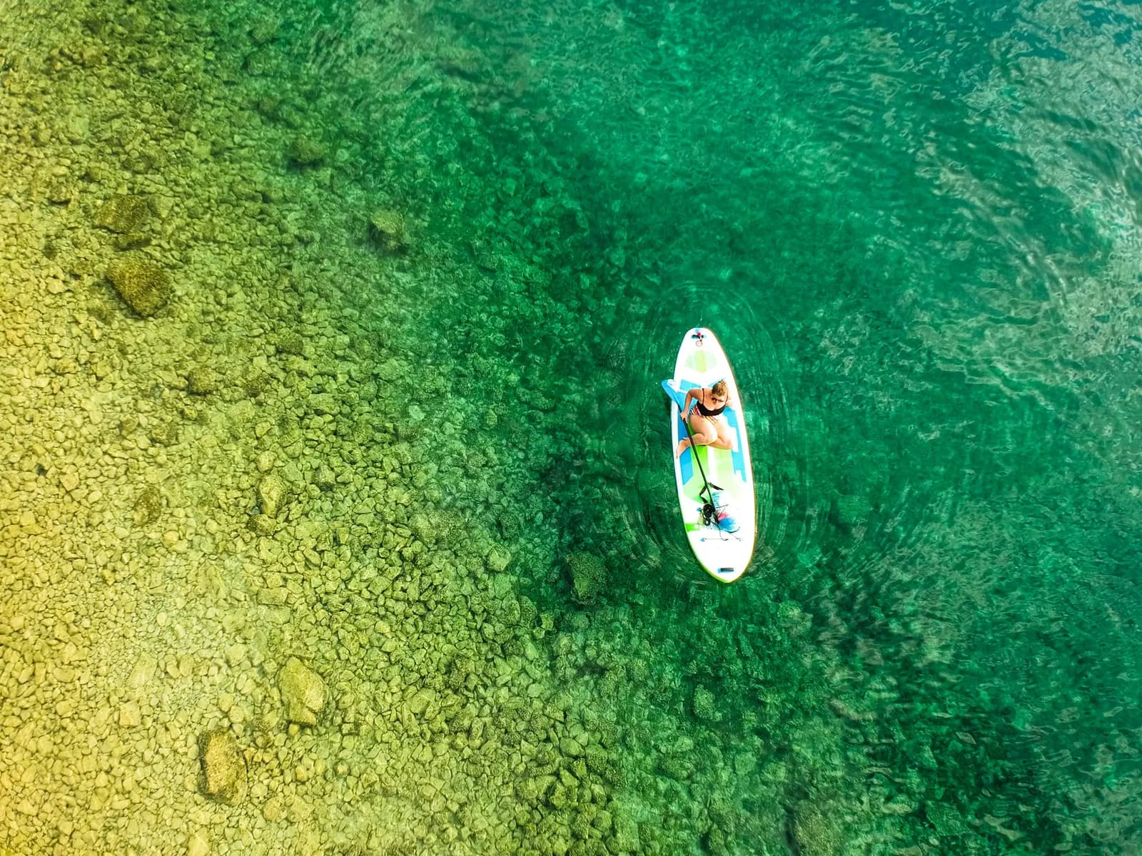 Paddleboarding over clear water and a rocky seabed, aerial view