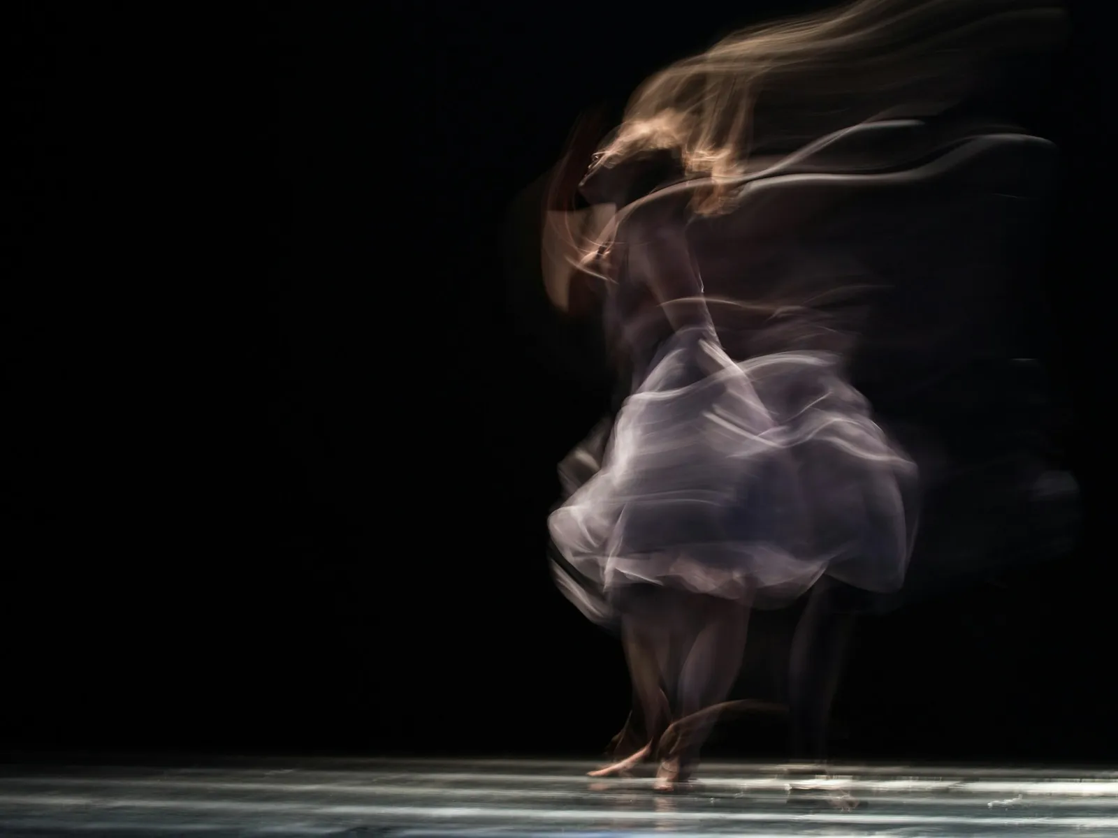 Bailaora de flamenco en movimiento sobre un escenario en penumbra (imagen ilustrativa)