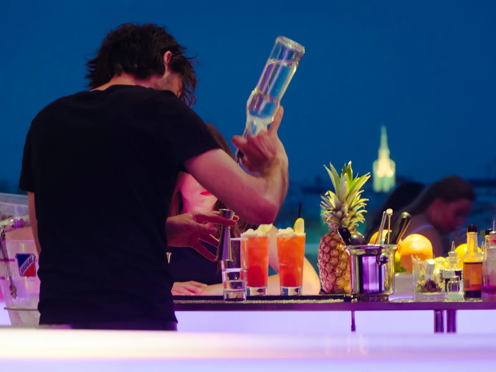 Bartender mixing cocktails at a rooftop bar at dusk