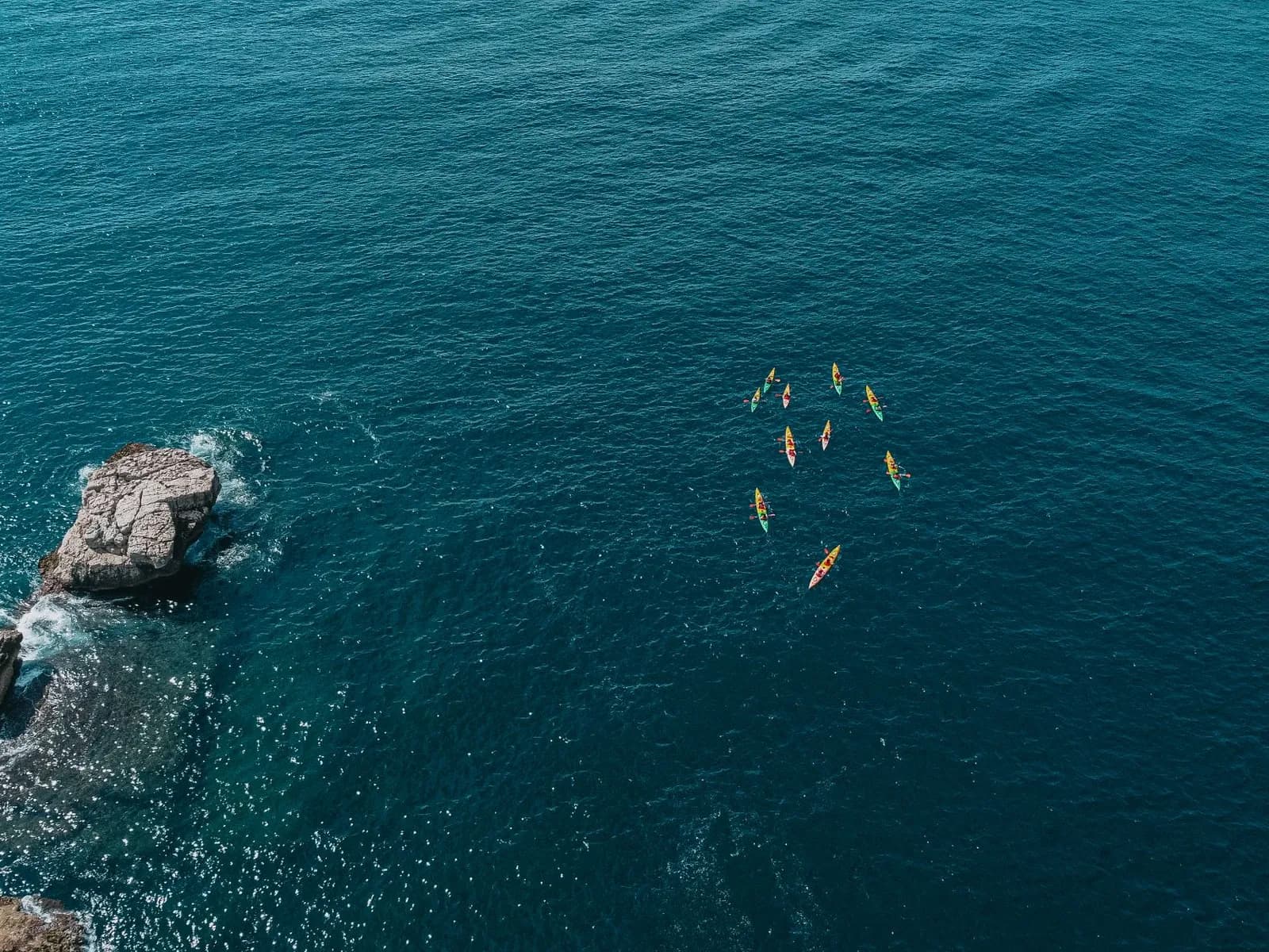 Grupo de kayaks remando junto a una costa rocosa, vista aérea