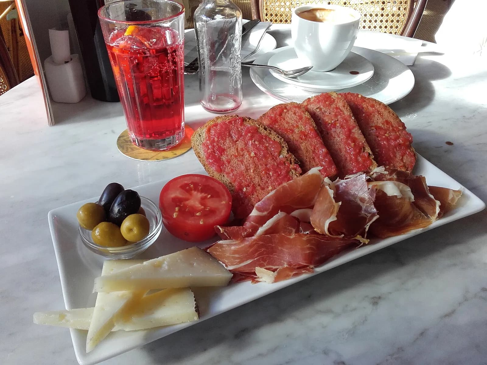 Tapas con embutido, queso y aceitunas acompañadas de una bebida