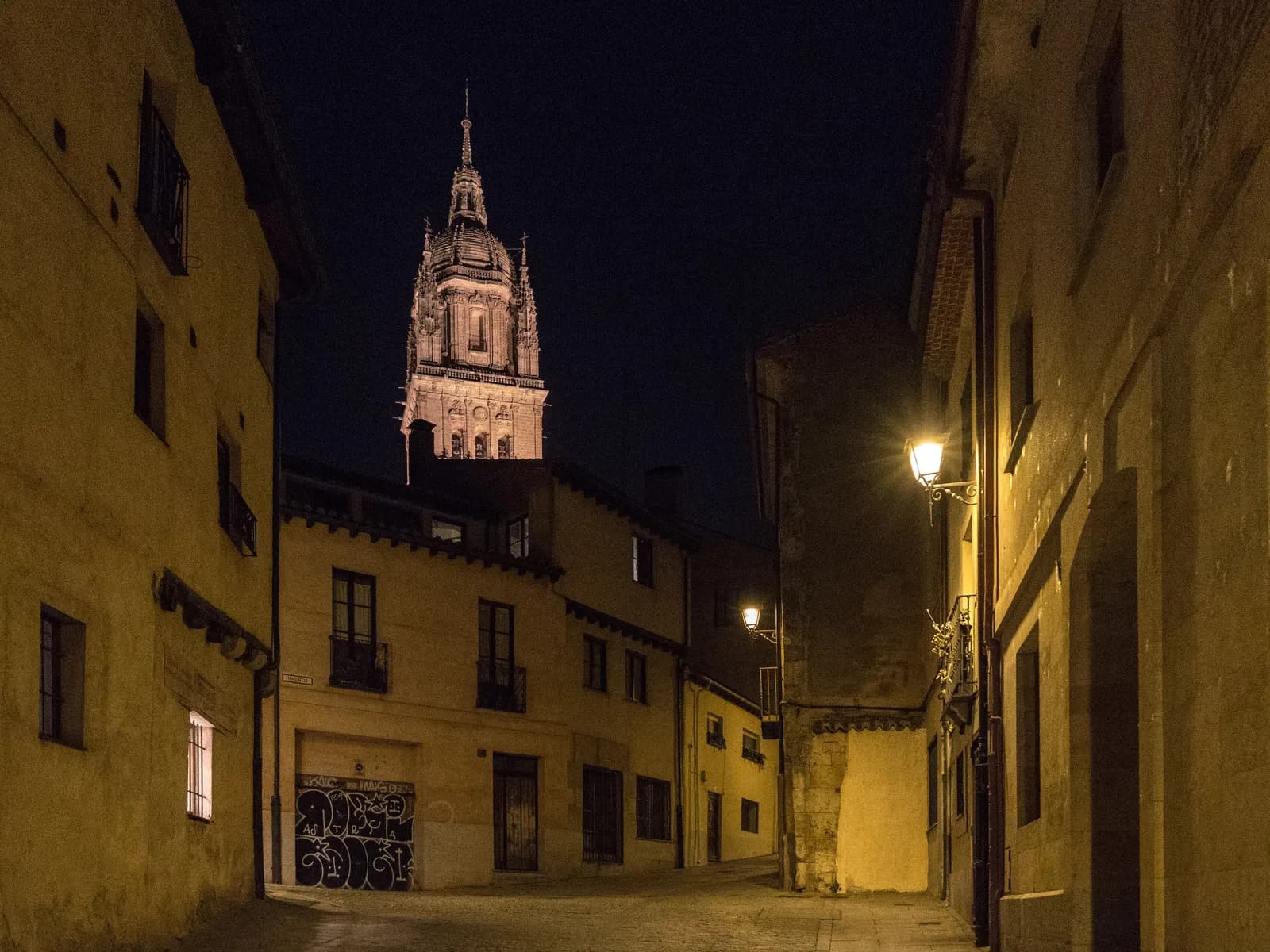 Calle del casco antiguo de Salamanca de noche con una torre iluminada al fondo