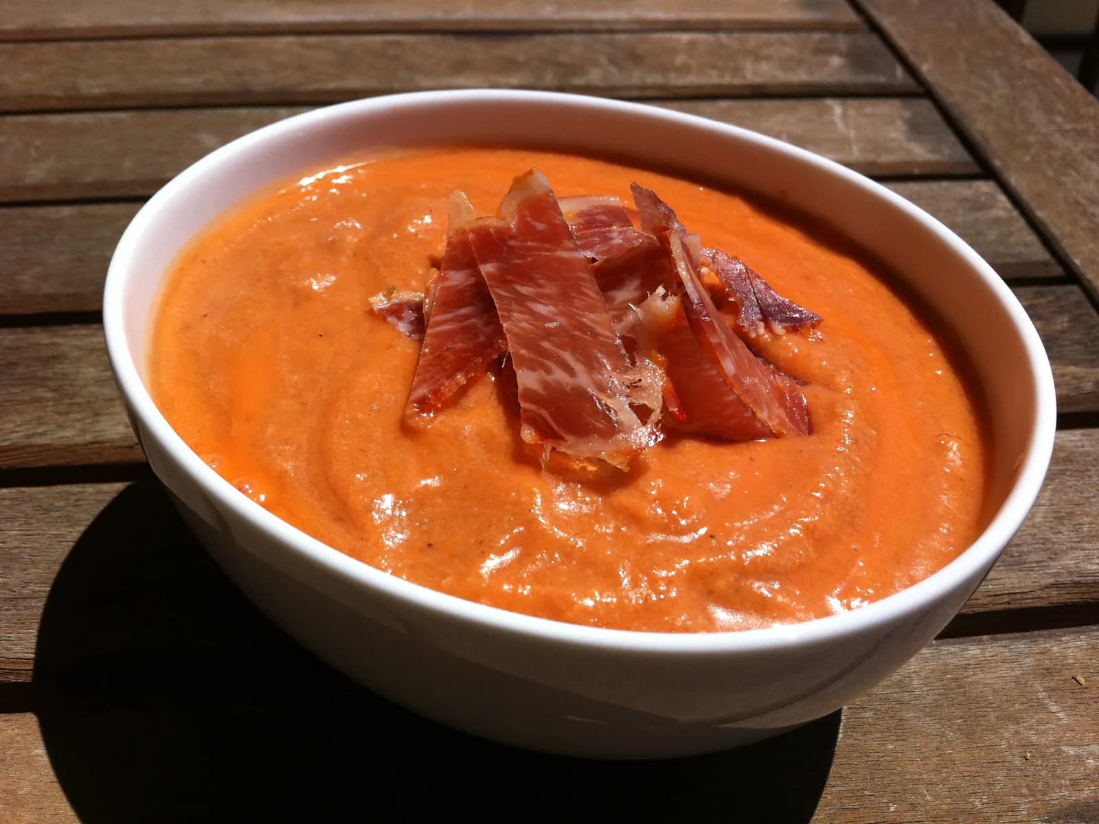 Cuenco de salmorejo con virutas de jamón sobre una mesa de madera