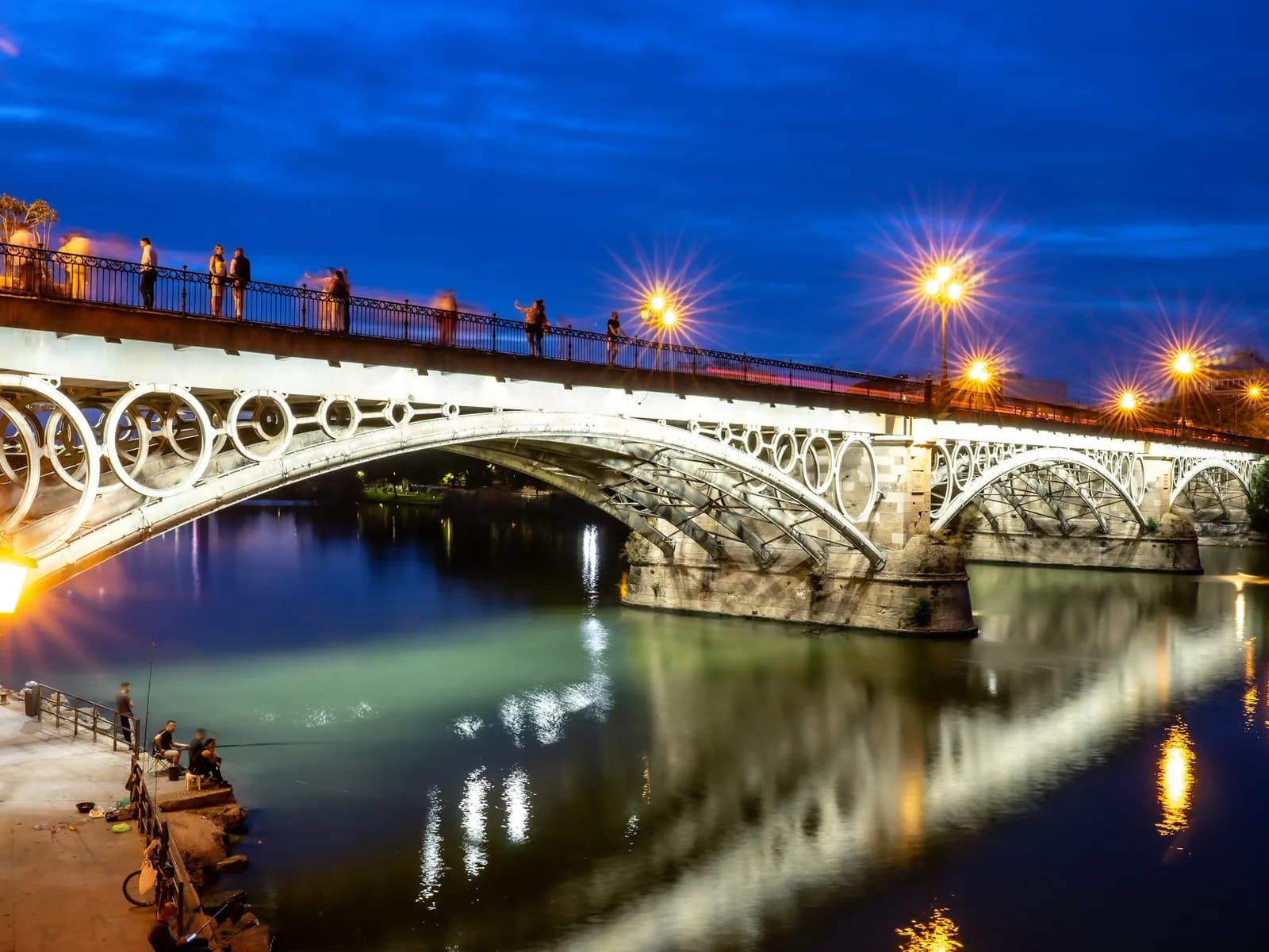 The Isabel II (Triana) Bridge lit up at night and reflected in the Guadalquivir