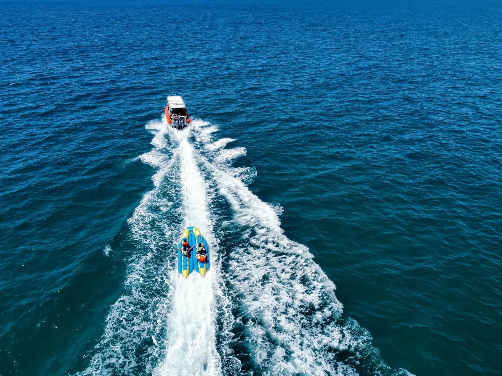 Speedboat towing a banana boat on the open sea, aerial view