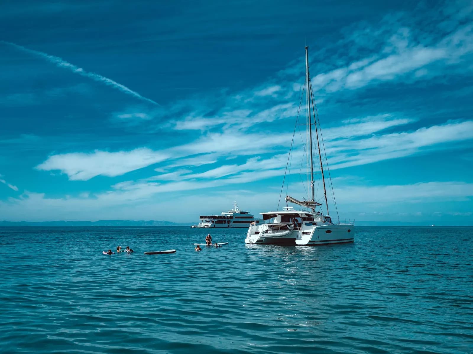 Catamarán fondeado en mar abierto con gente bañándose a su alrededor