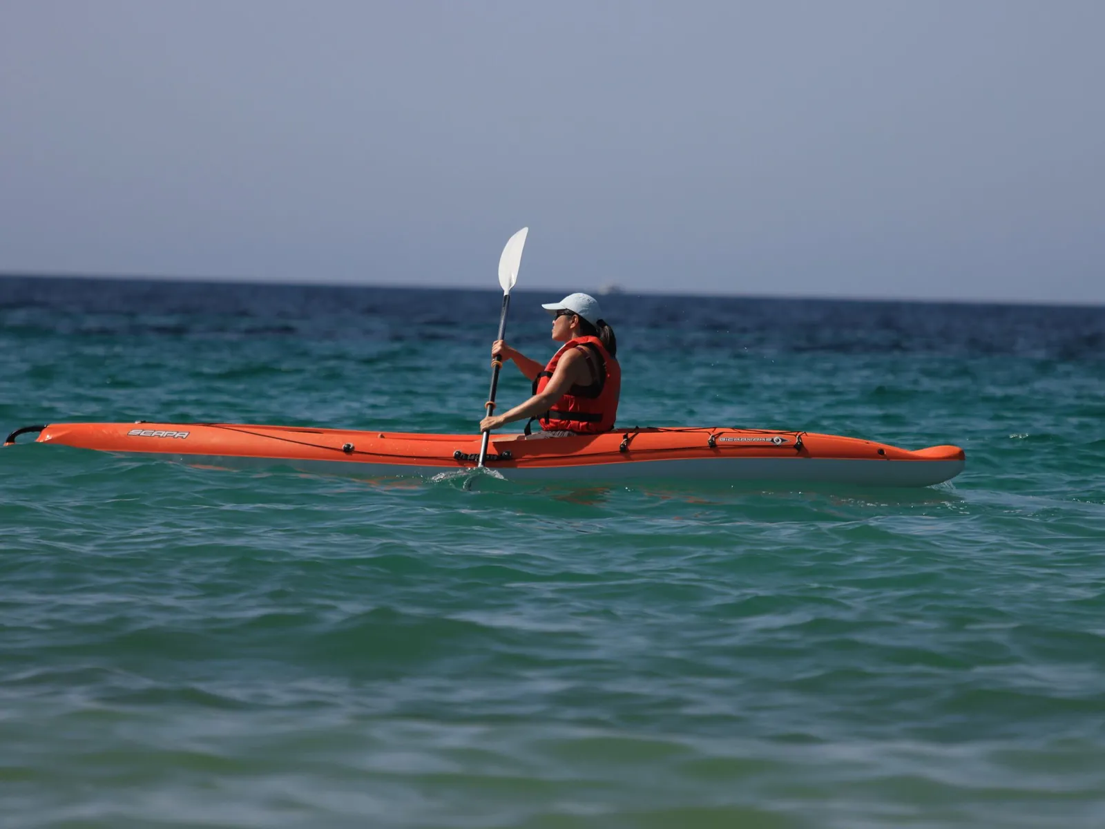 Persona remando en un kayak naranja en mar abierto