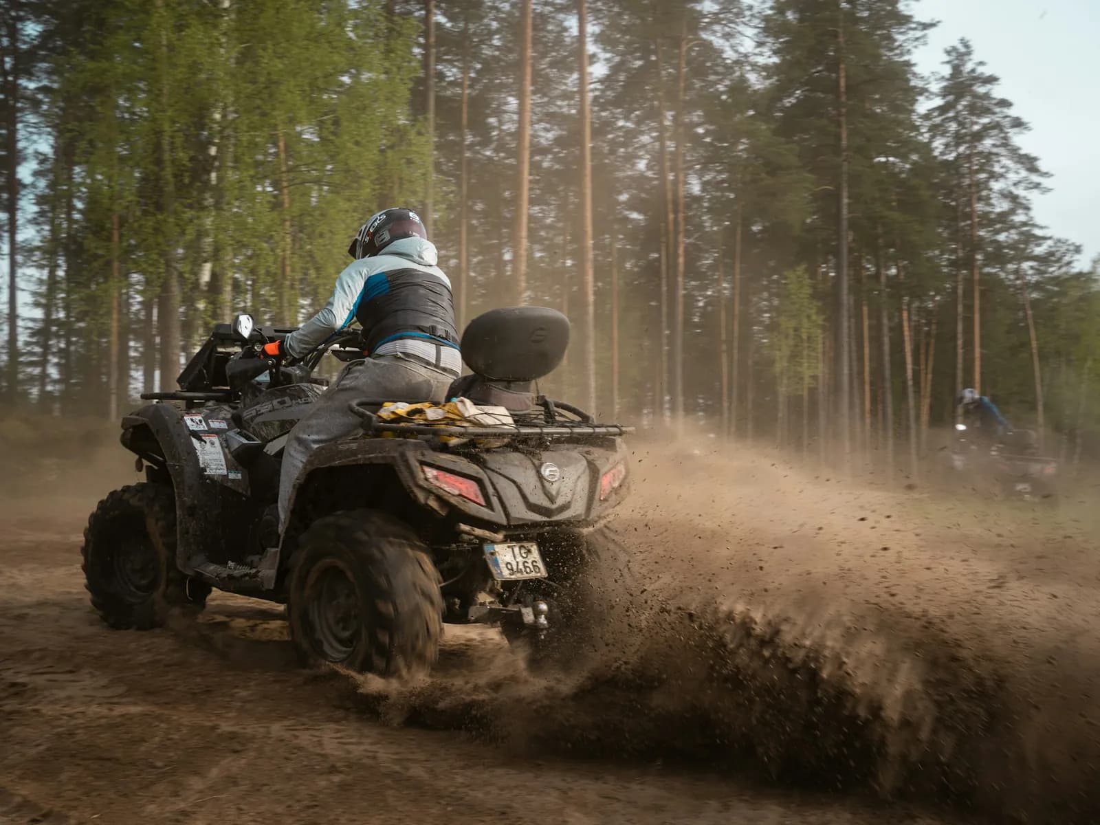Quad bike kicking up dust on a dirt track through pines