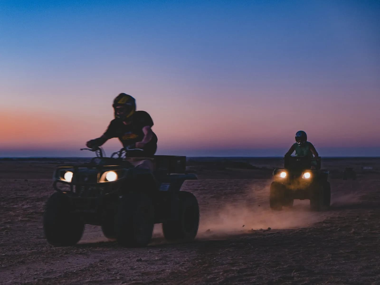 Two quad bikes with headlights on at dusk